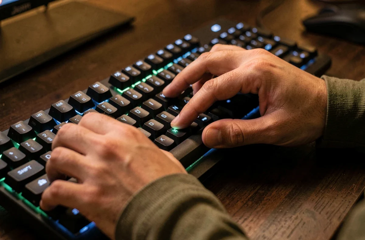 Gros plan des mains sur un clavier mécanique rétroéclairé avec le doigt sur la touche Shift pour écrire en majuscule