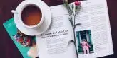 opened book with pink flower on top near filled ceramic mug