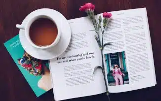 opened book with pink flower on top near filled ceramic mug