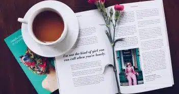 opened book with pink flower on top near filled ceramic mug